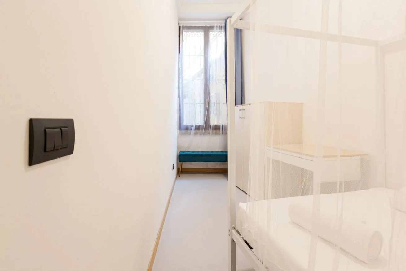 A bright bedroom with a bed behind a sheer partition and a window at the far end.