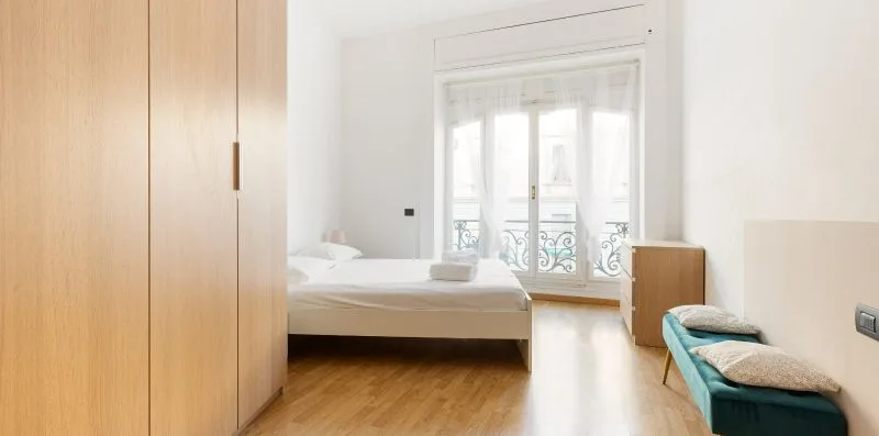 A bright bedroom with a bed, wooden wardrobes, and a small seating area.