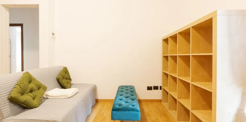 A bright room with a bed, a turquoise bench, and open wooden shelving.