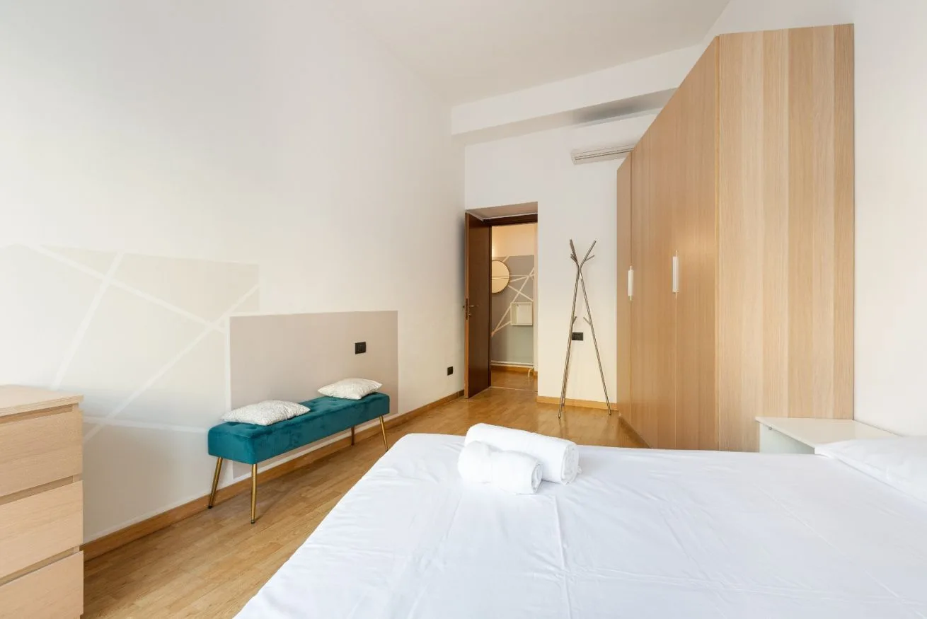 A bedroom with a bed, a teal bench, and wooden wardrobes.