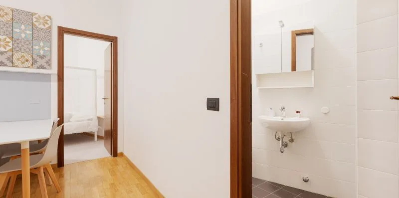 A bathroom sink and mirror are visible beside a doorway to a bedroom.