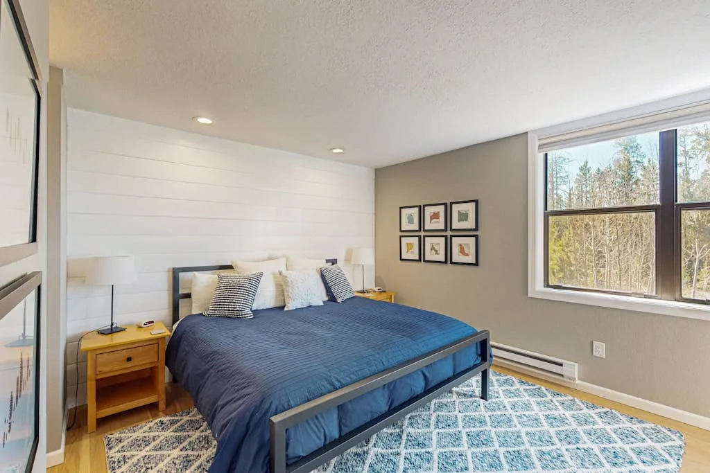 A bedroom with a blue bed, bedside tables, and a large window.