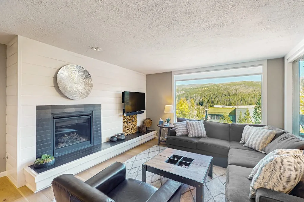 A bright living room with gray seating, a coffee table, and a wide window.