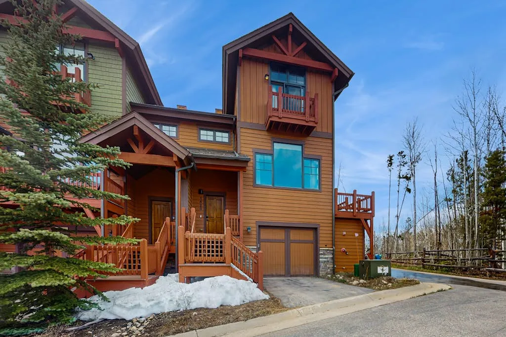 A multi-story house with wooden siding, balconies, and snow along the driveway.