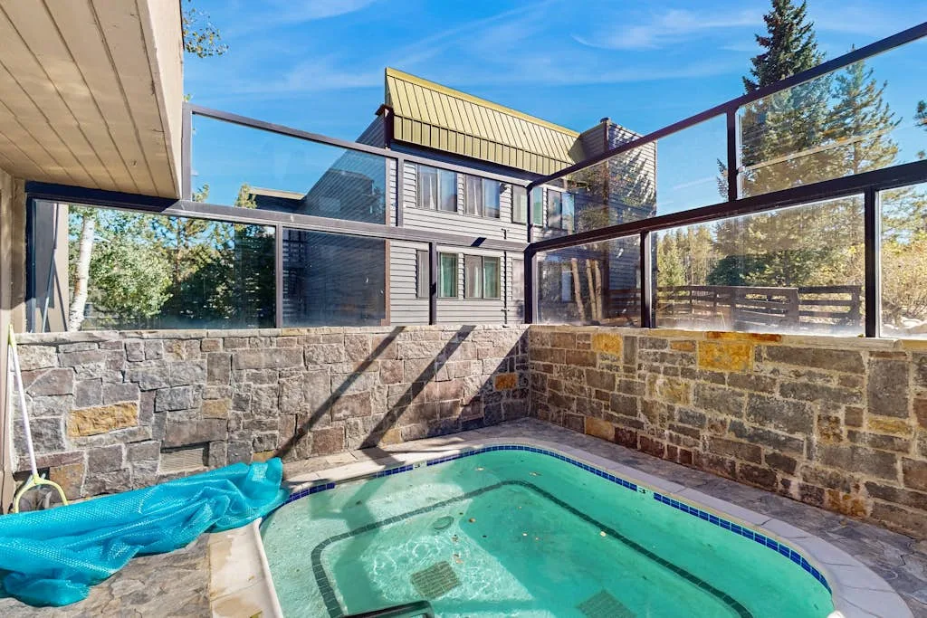 An outdoor swimming pool sits beside a stone wall and glass railing.