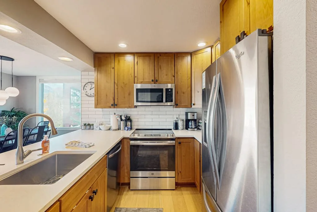 A kitchen with wooden cabinets, a stainless steel refrigerator, and a central cooking range.