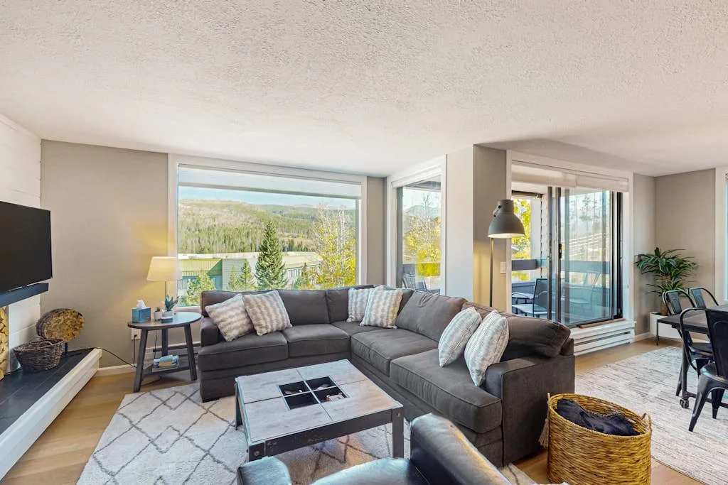 A living room with a sectional seating area beside large windows.
