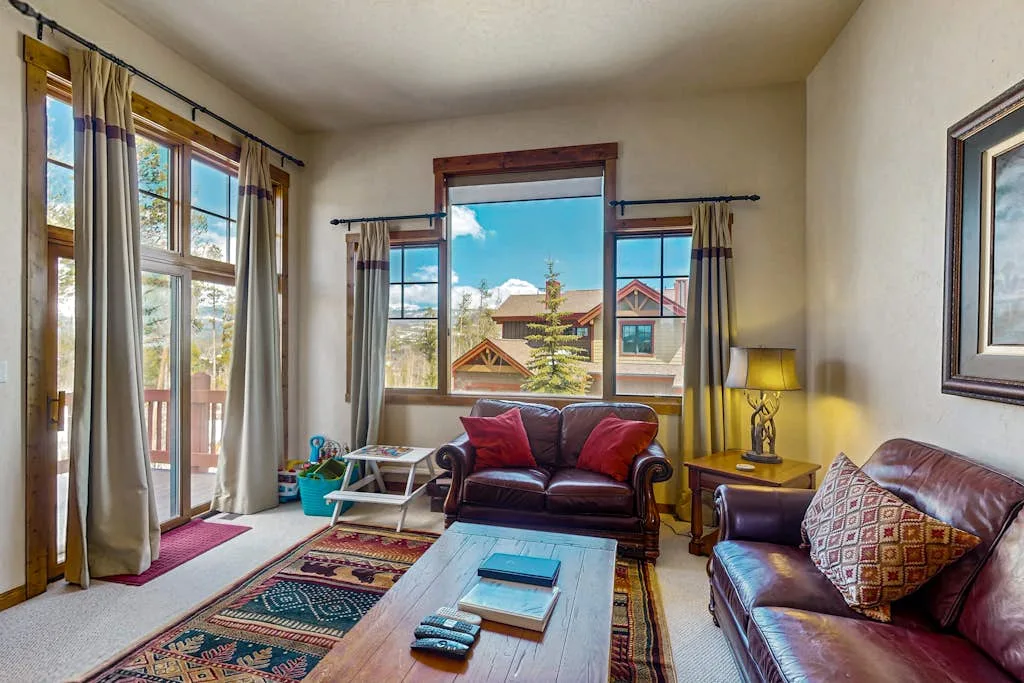 A living room with leather seating, a coffee table, and several large windows.