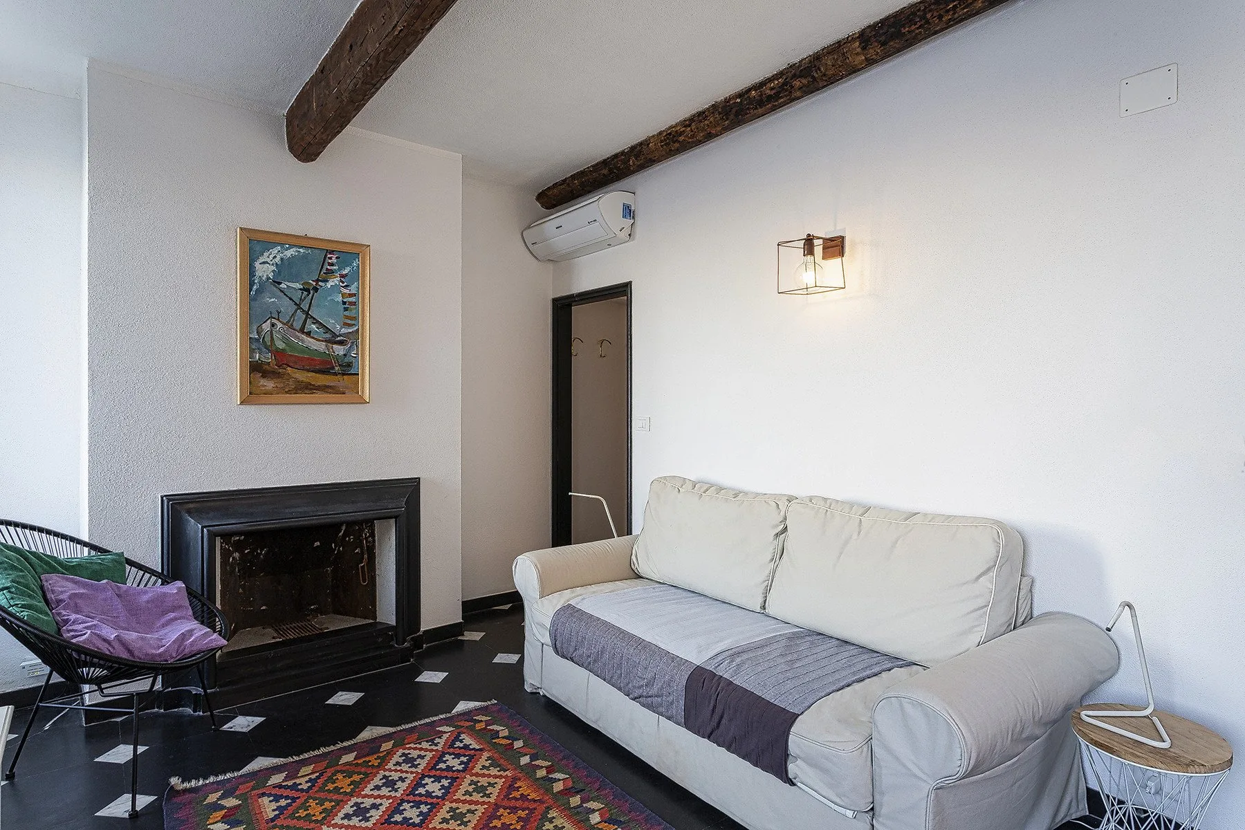 Una sala de estar con sofá claro, chimenea y alfombra estampada.