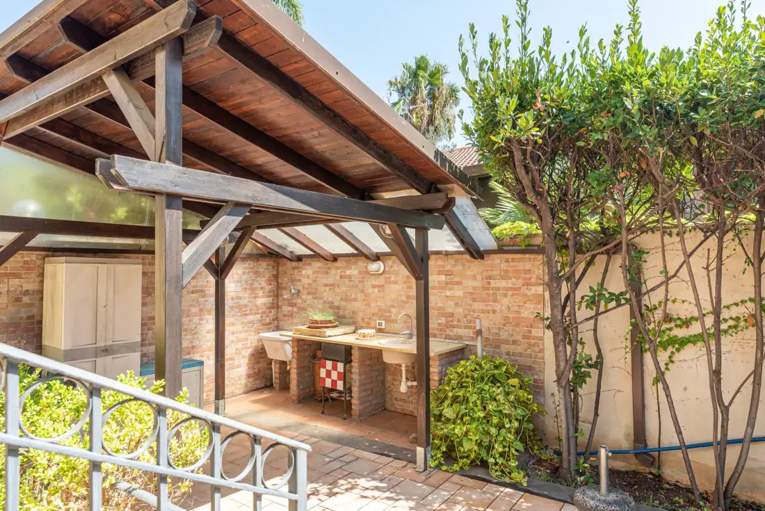 Una cocina exterior cubierta con una encimera de ladrillo y plantas frondosas.