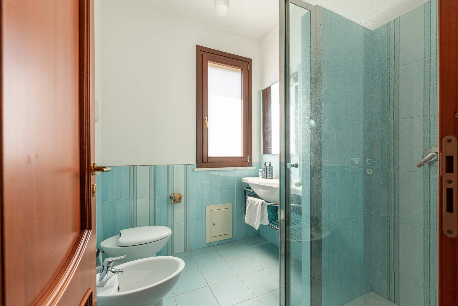 Un baño alicatado con inodoro, lavabo y ducha de vidrio.
