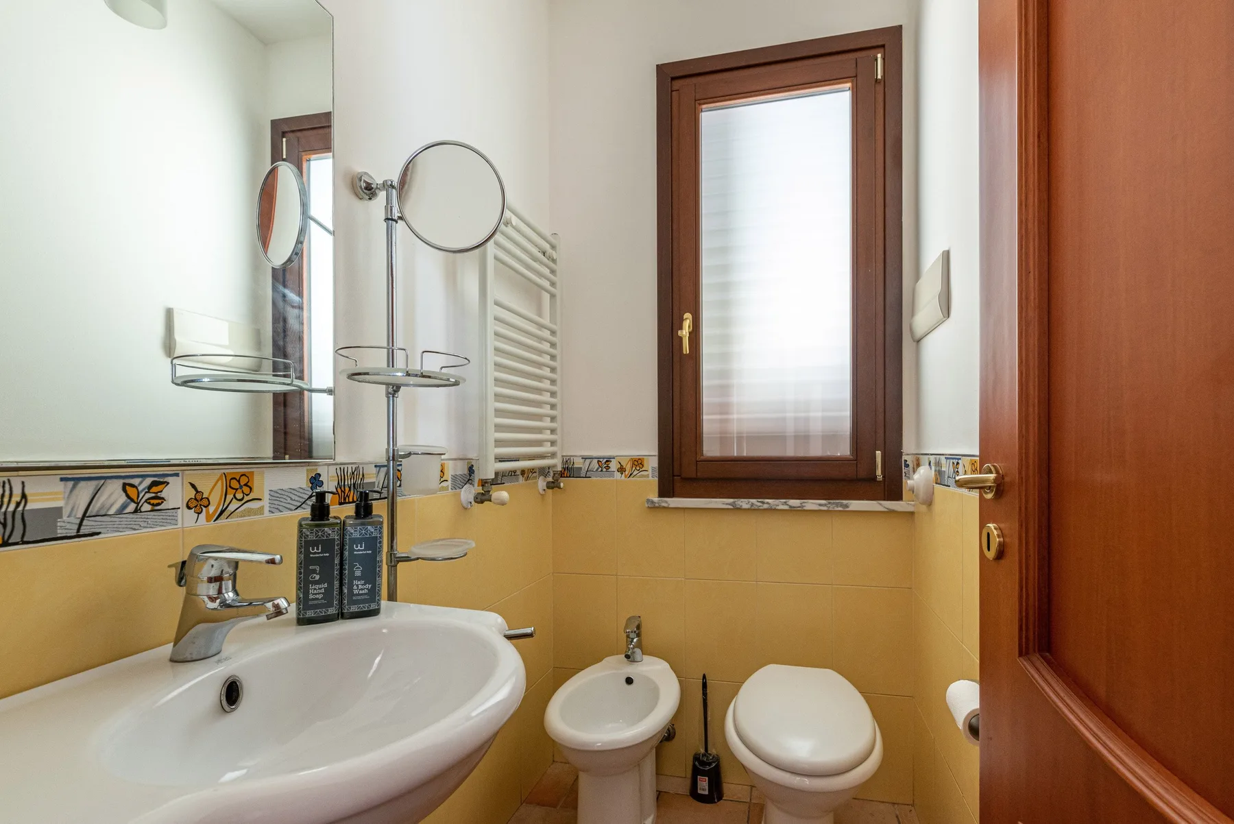 Un baño con lavabo, bidé e inodoro bajo una ventana.