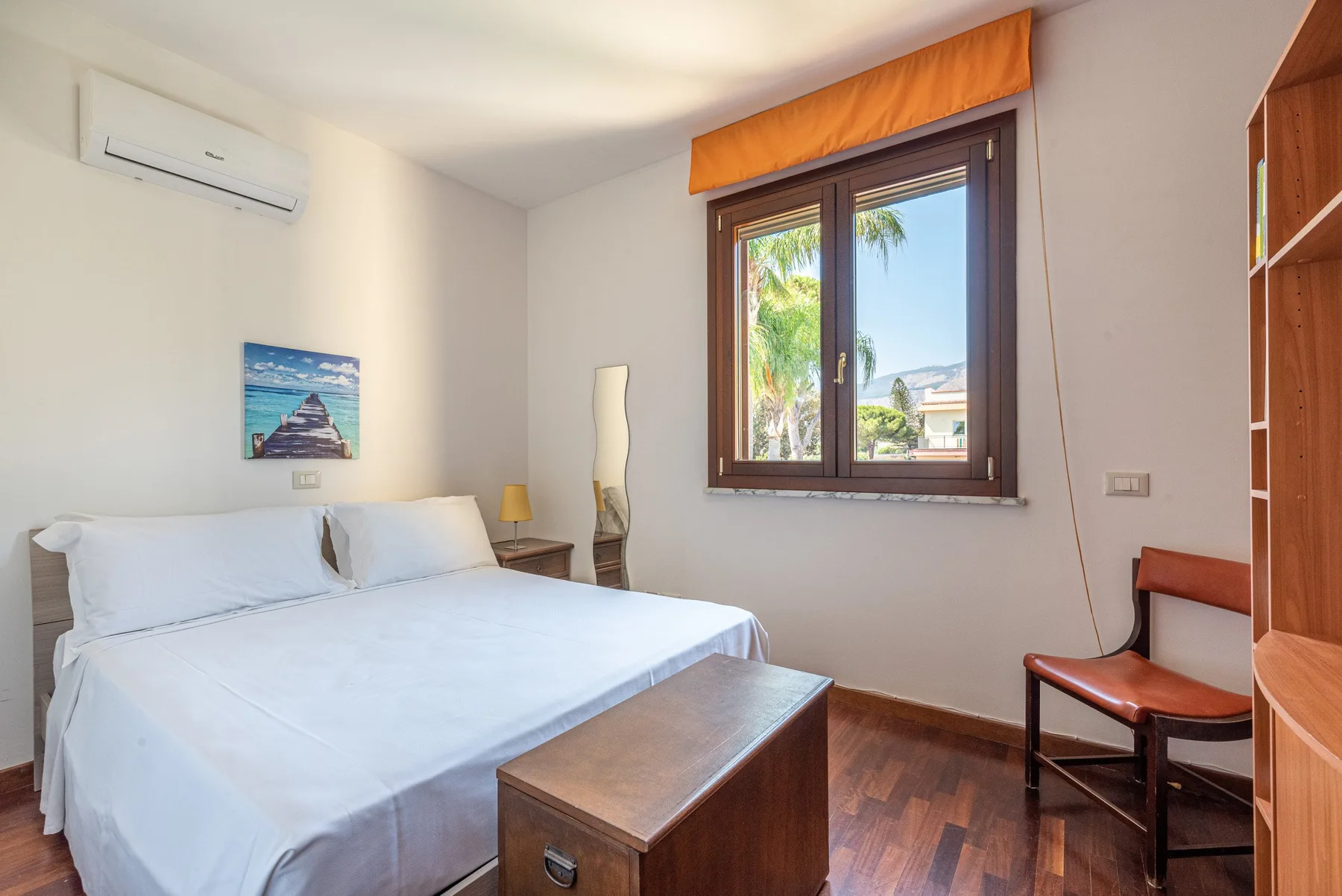 Un dormitorio con una cama, una mesa de madera y una ventana con vistas a palmeras.