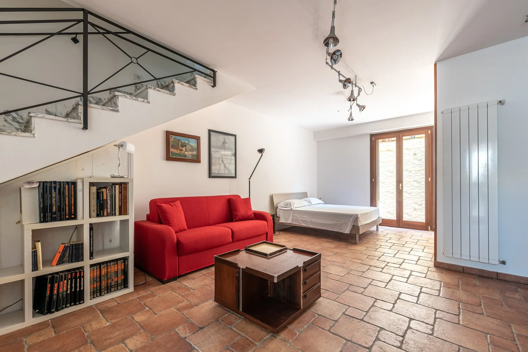 Una luminosa sala de estar con asientos rojos, una cama y suelo de baldosas.