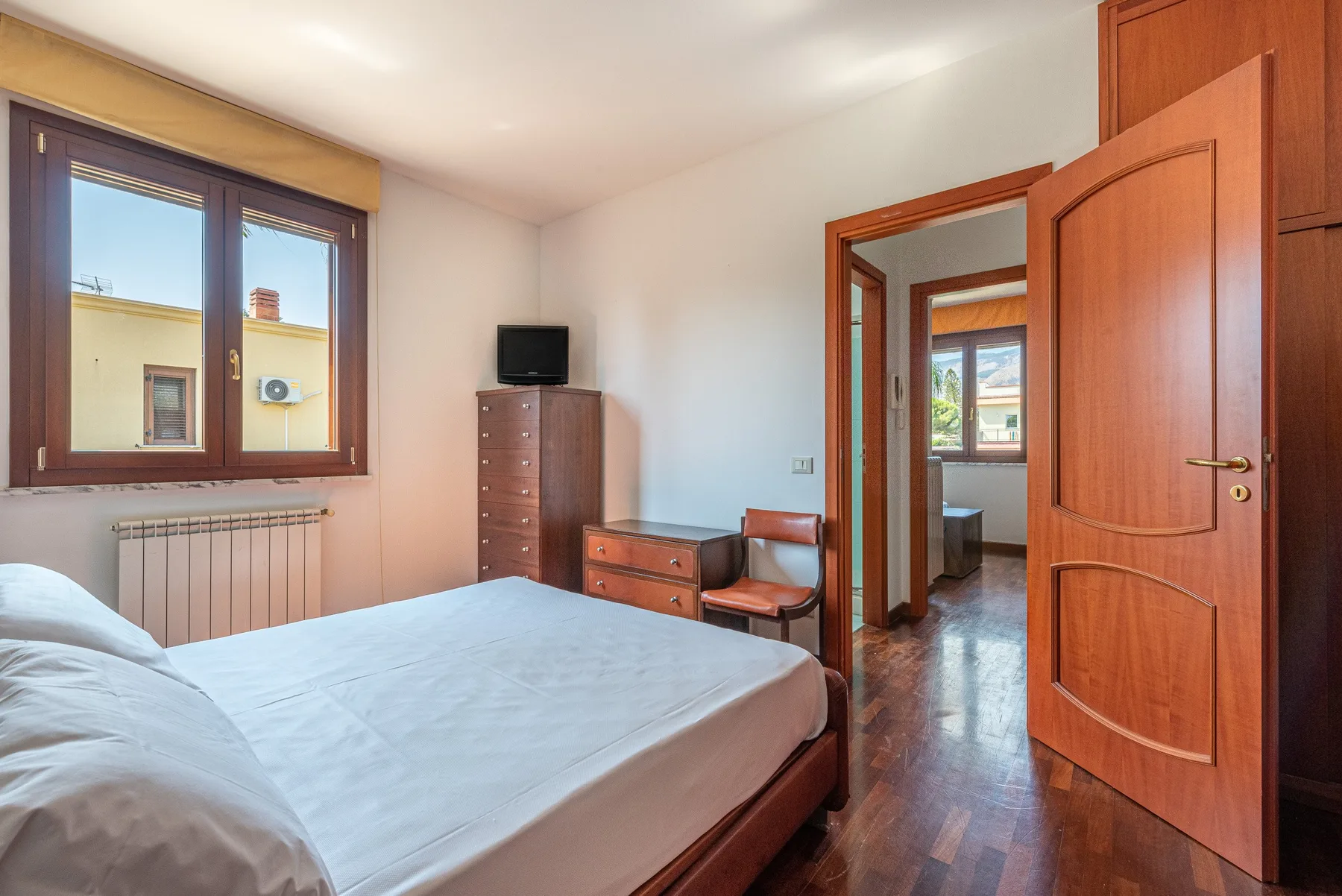 Un dormitorio con una cama, una ventana y una puerta de madera abierta.