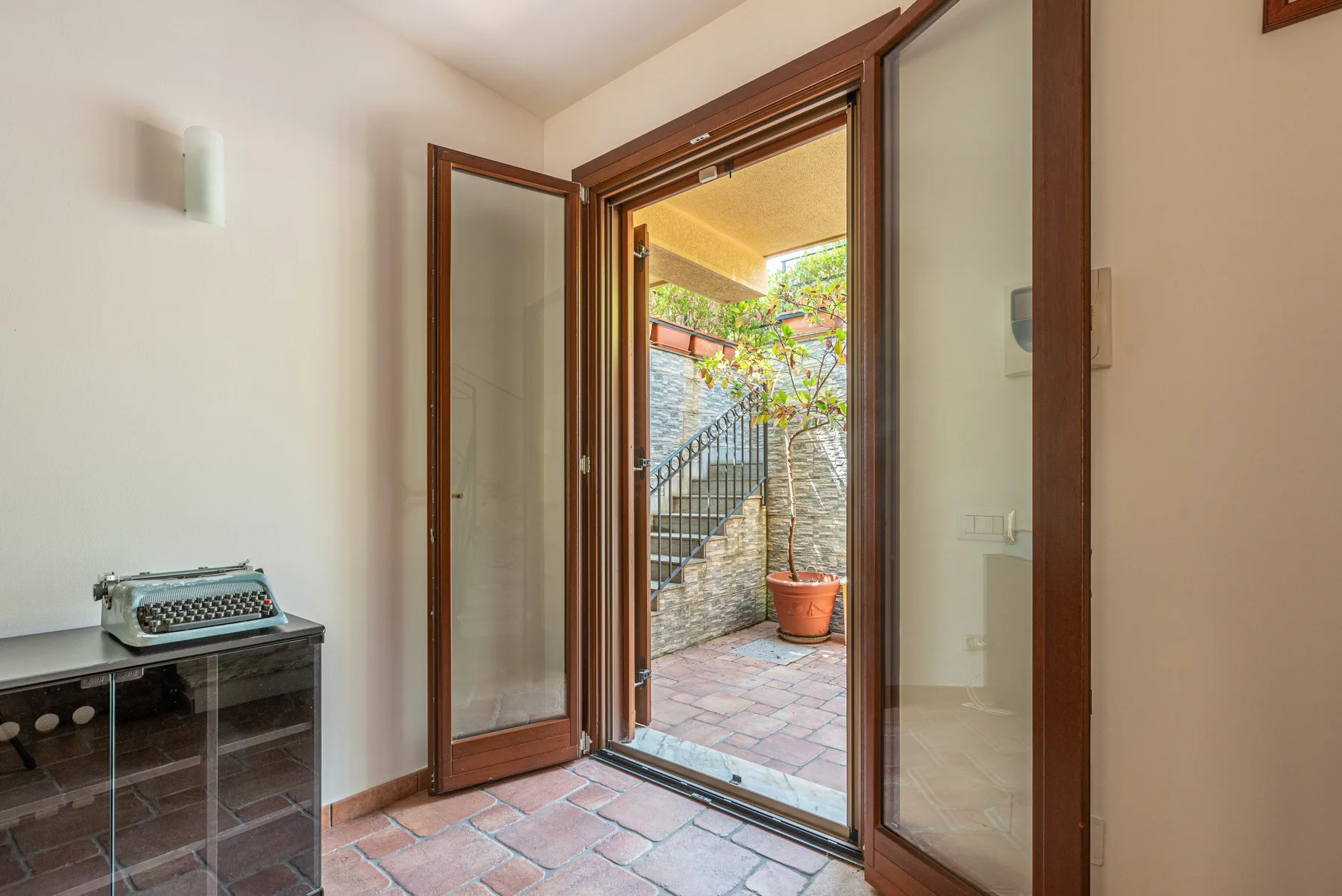Una entrada con suelo de baldosas se abre a un patio exterior con una planta en maceta.