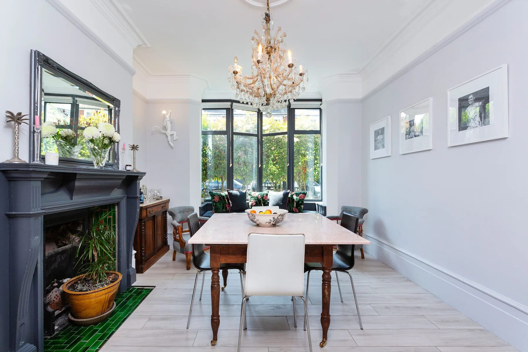 A bright dining room with a long table, dark fireplace, and large windows.