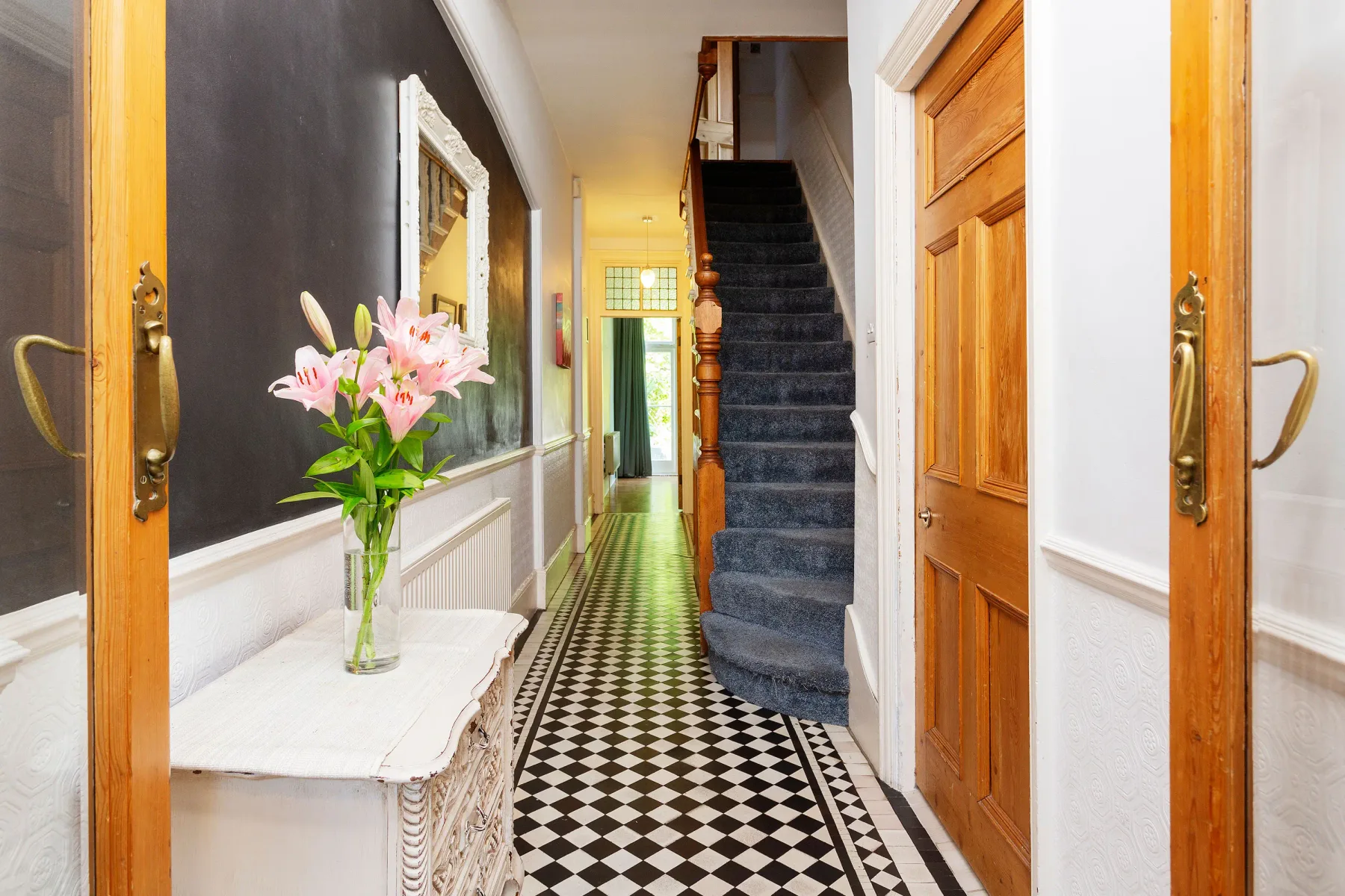 A hallway with a patterned tile floor, wooden doors, and a staircase.