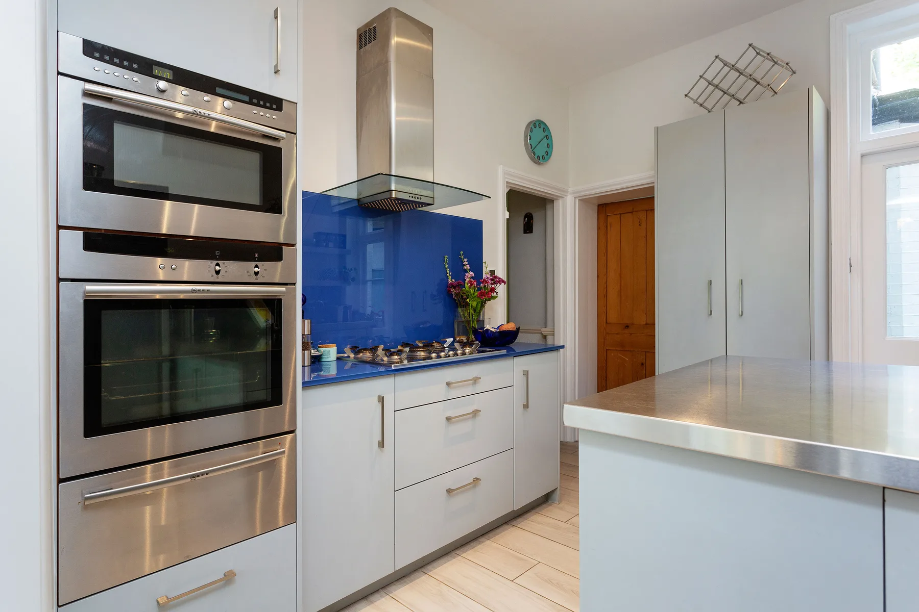 A bright kitchen with built-in ovens, blue backsplash, and a central island.
