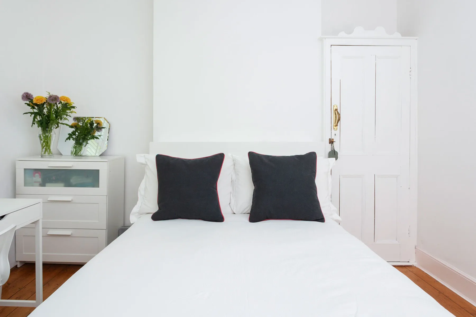 A bright bedroom with a bed and dark accent pillows.
