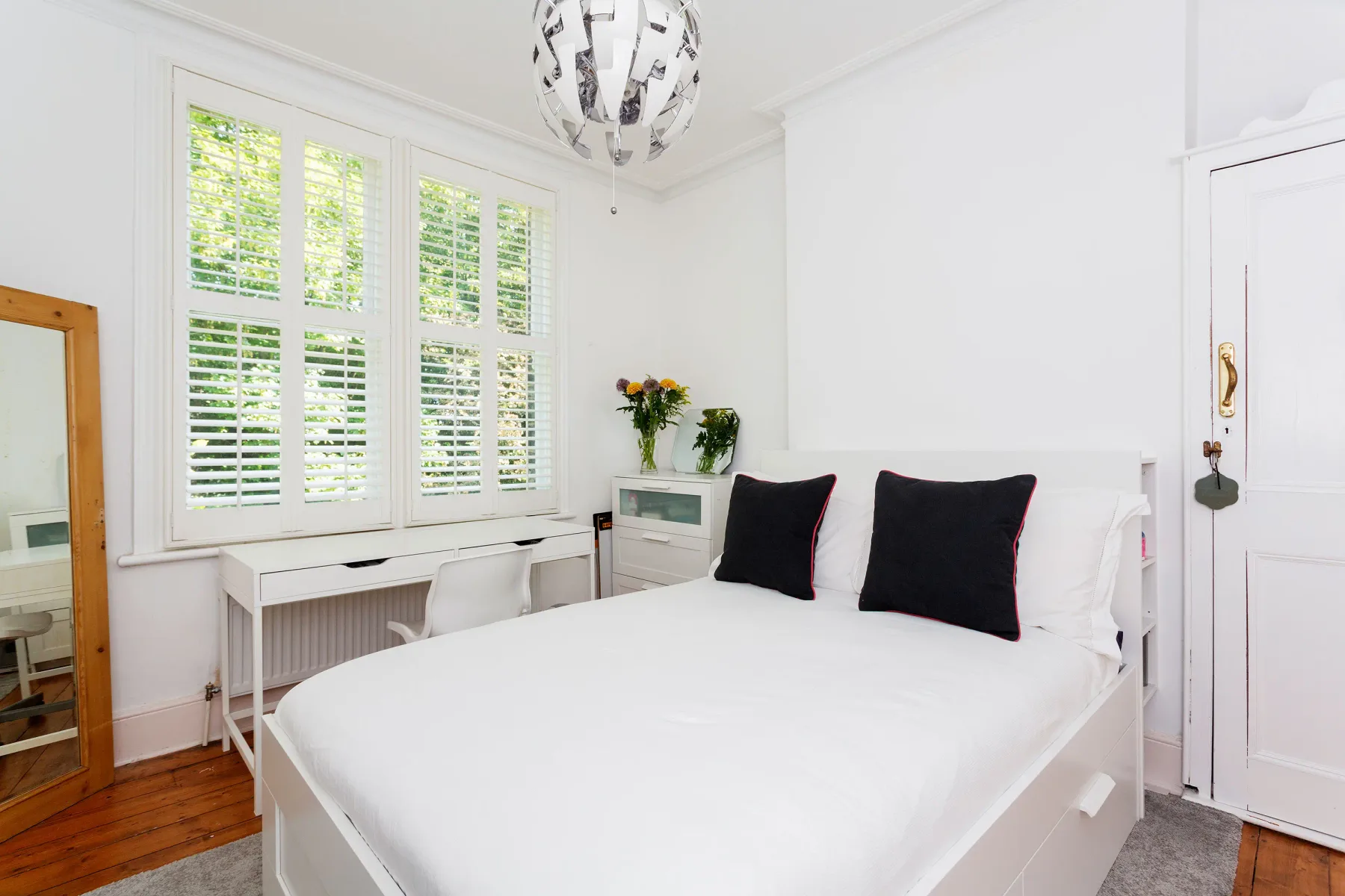 A bright bedroom with a white bed beneath large shuttered windows.