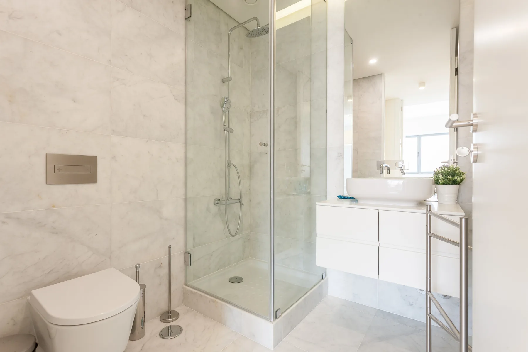 Un baño luminoso con una ducha de cristal y un lavabo blanco.