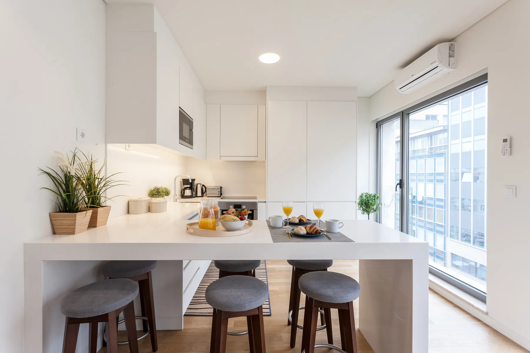 Cocina y comedor luminosos con una barra, taburetes y ventanales.