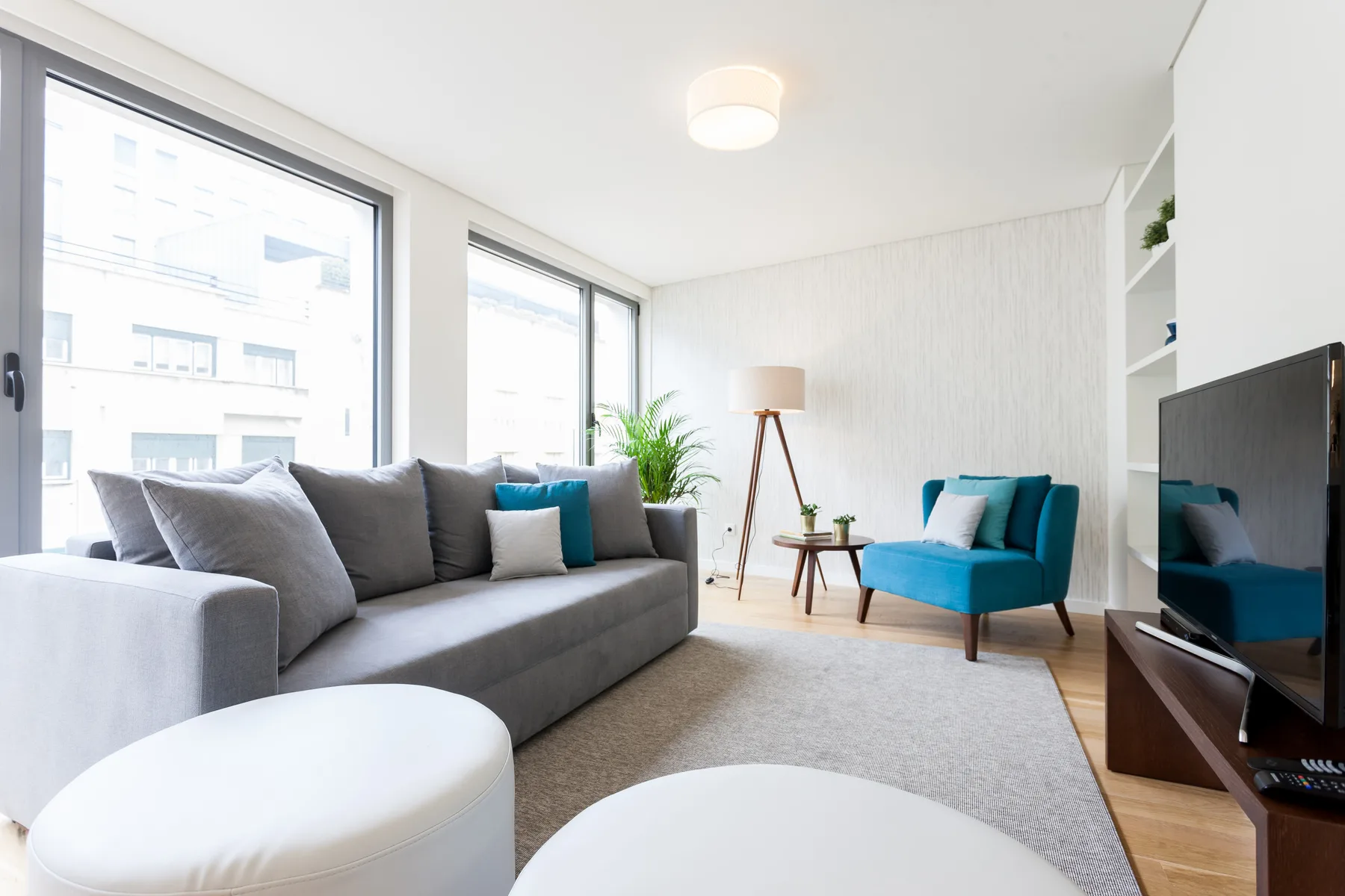Una sala luminosa con asientos grises, un sillón turquesa y ventanales.