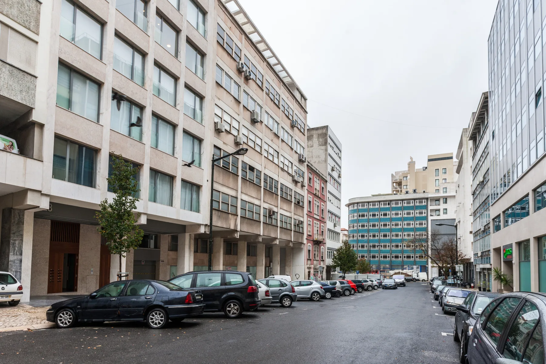 Una calle urbana está flanqueada por edificios de varias plantas y coches aparcados.