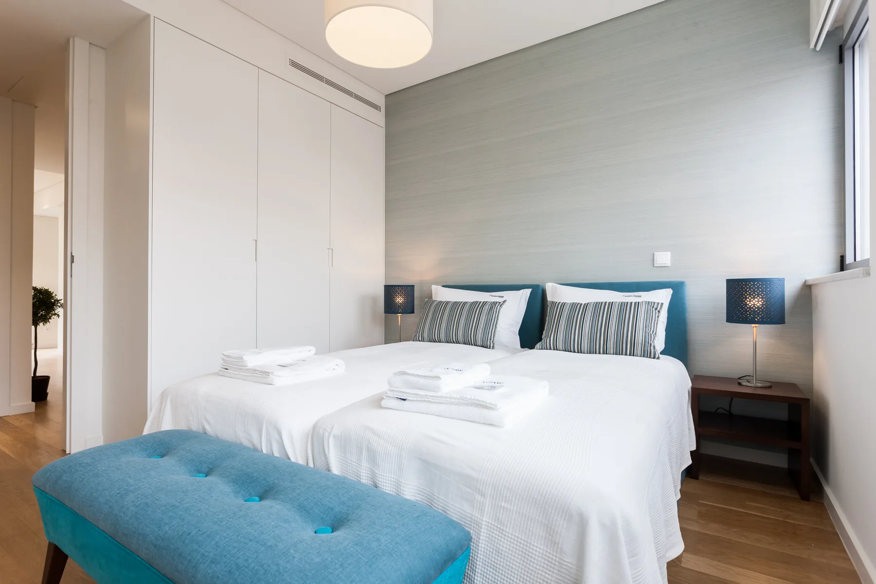 Un dormitorio con una cama bien hecha y un banco tapizado de color azul.