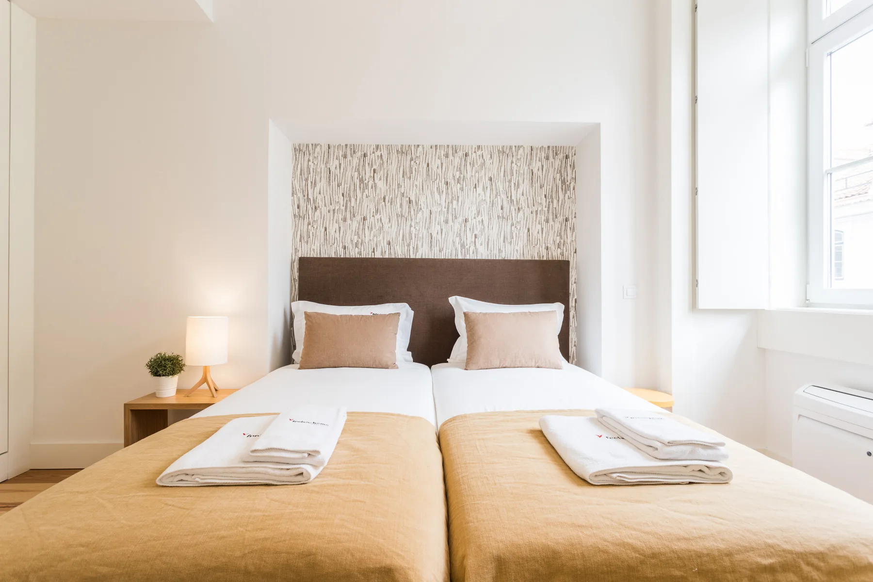 A bright bedroom with two beds, folded towels, and a large window.