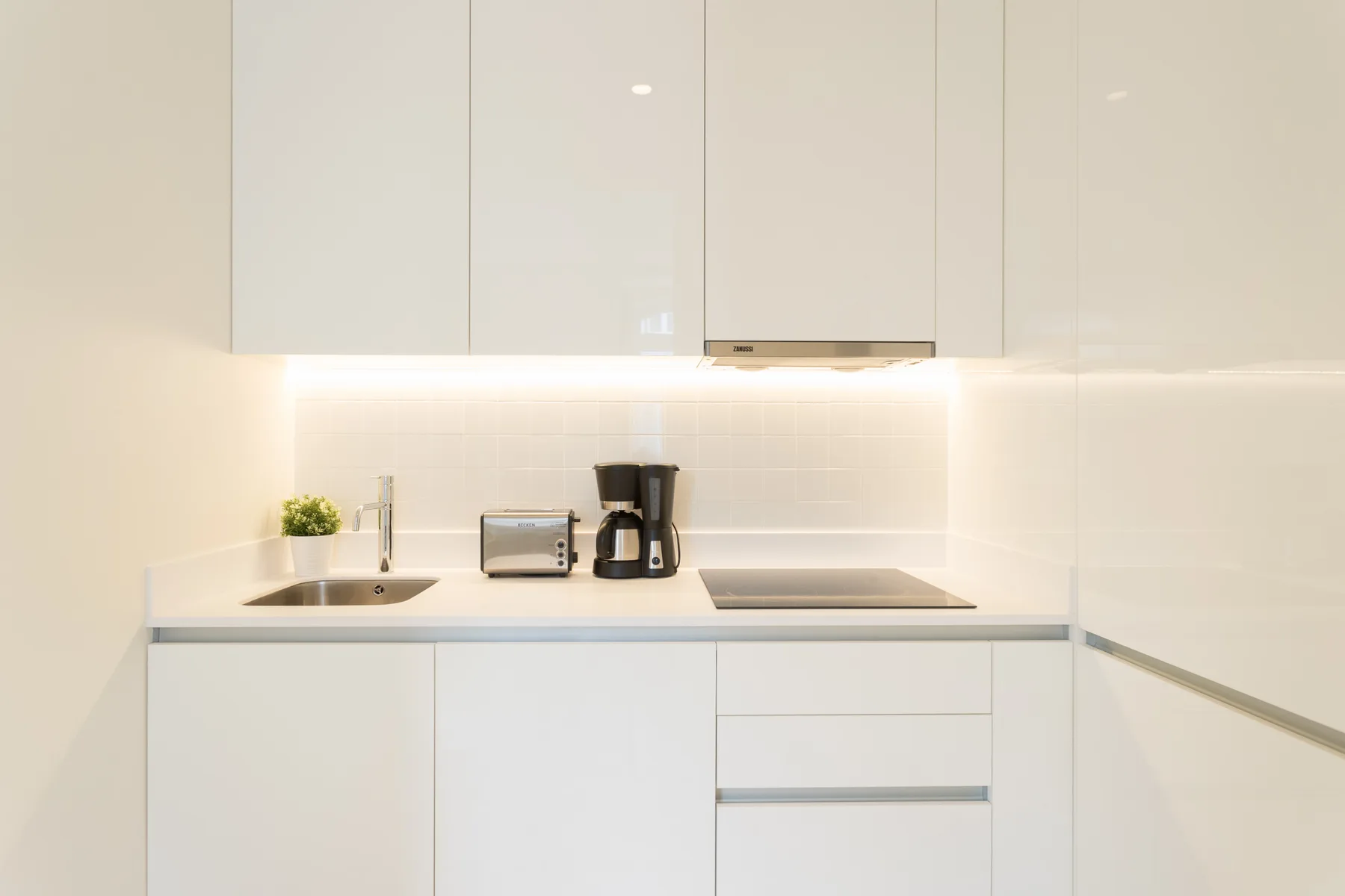 A modern kitchen with a sink, cooktop, and small appliances on the counter.
