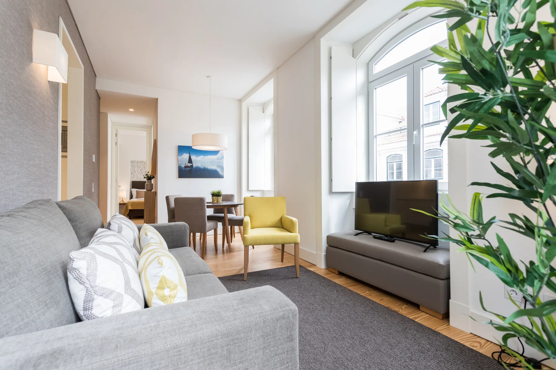 A bright living room with seating, a television, and tall windows.
