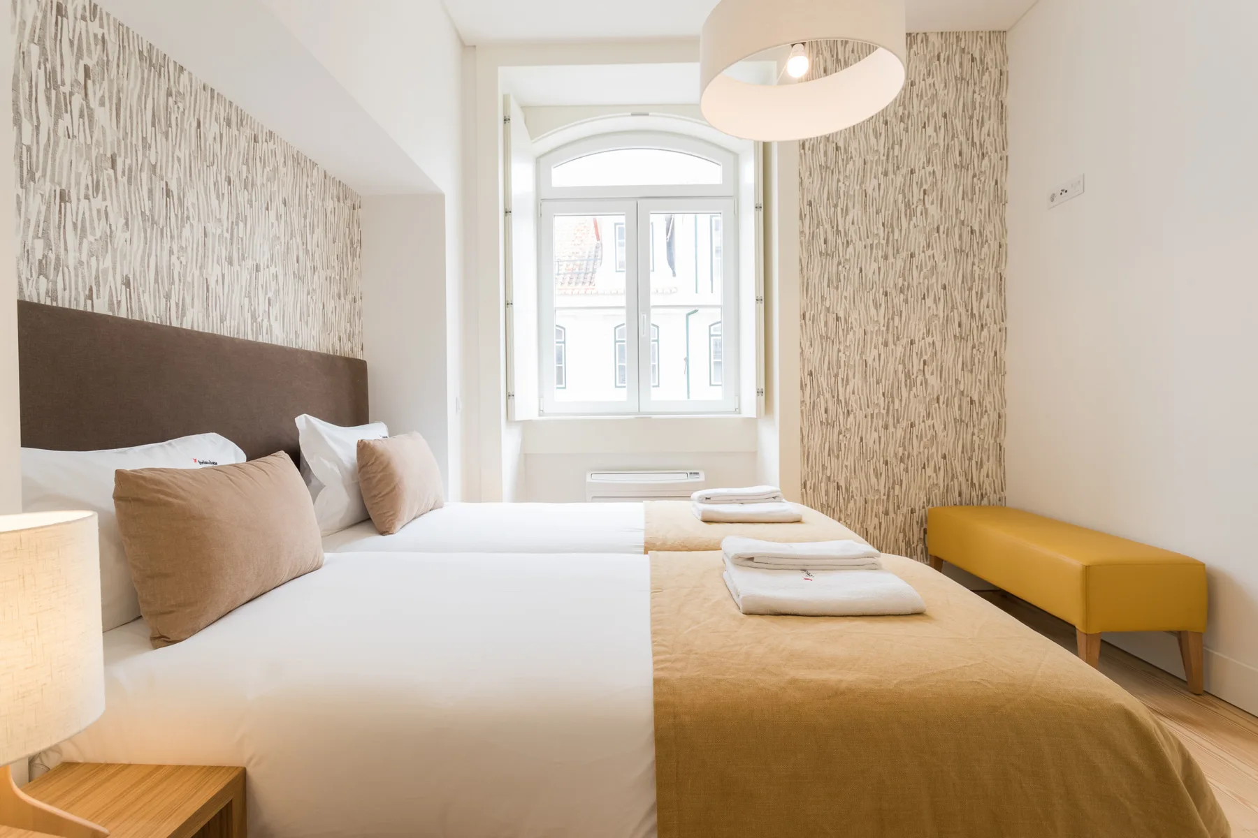 A bright bedroom with white bedding and a large window.