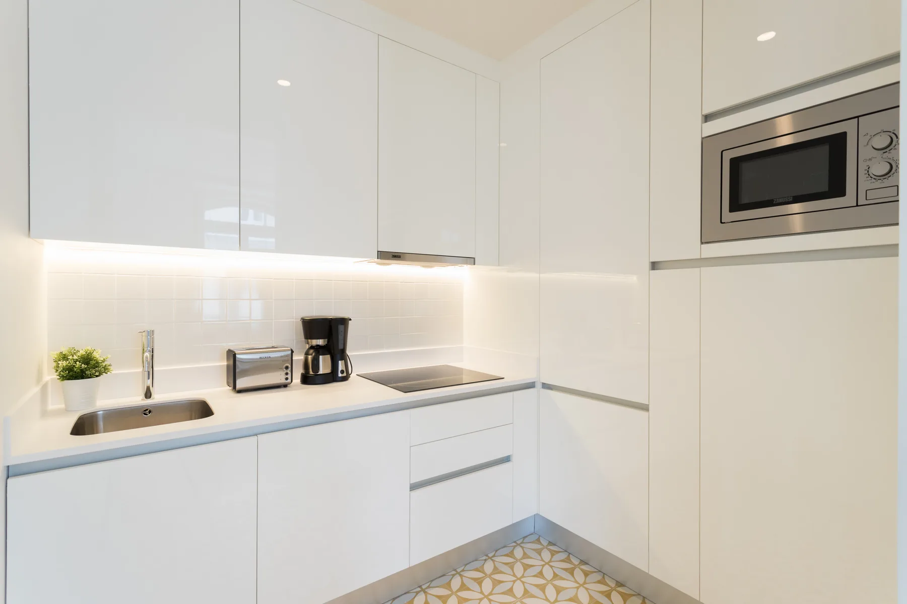 A bright white kitchen with a cooktop, sink, and built-in microwave.