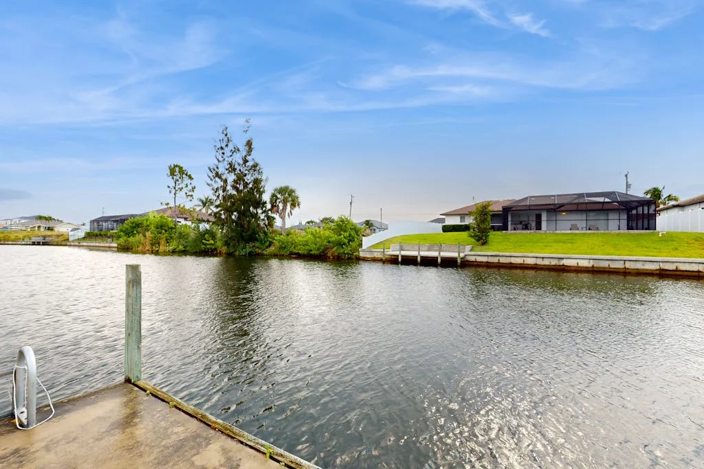 A waterside view shows a calm canal, grassy banks, and homes beneath a blue sky.