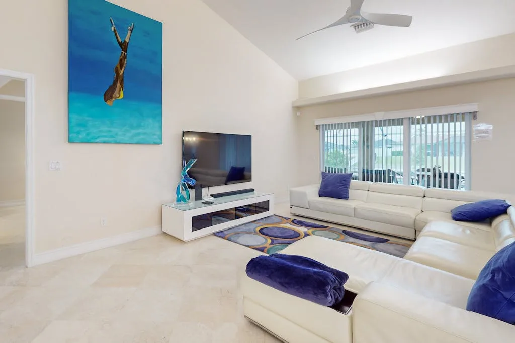 A bright living room with white seating, a television, and a large window.