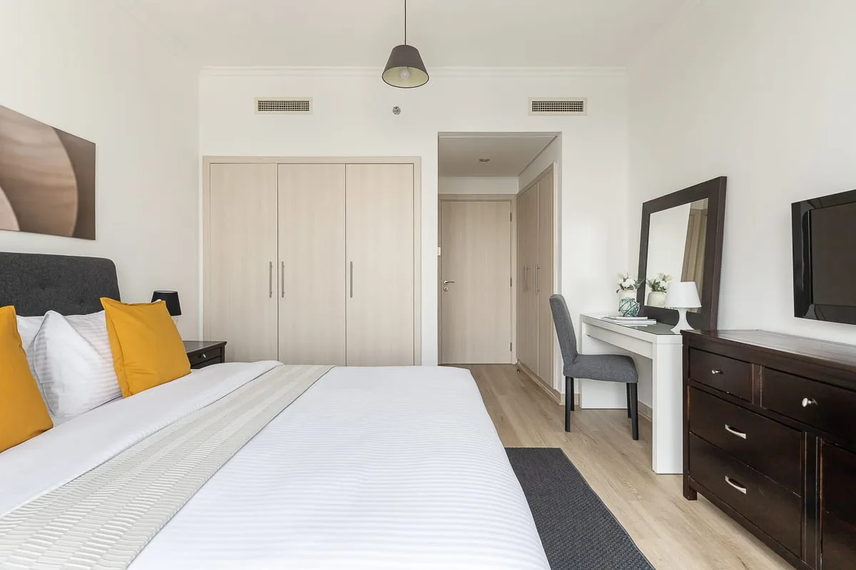 Un dormitorio luminoso con una cama bien tendida y un pequeño escritorio junto a la entrada.