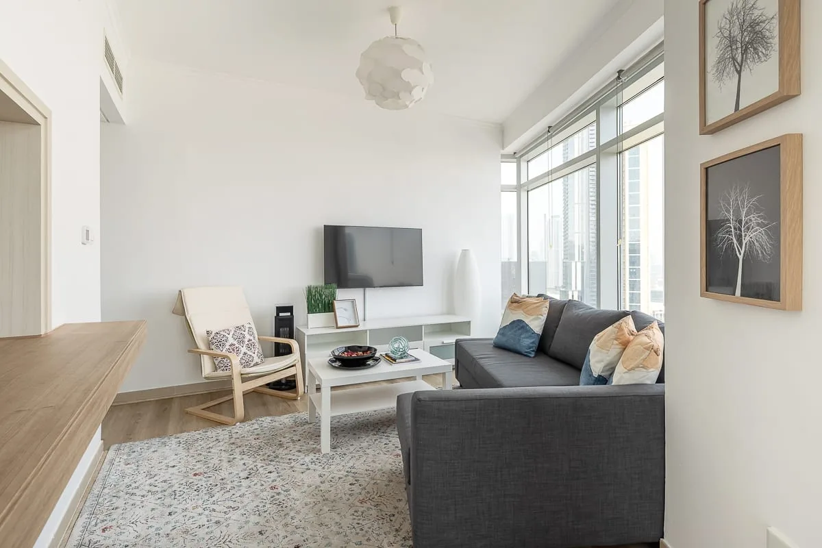 Una sala luminosa con un sofá seccional gris, una mesa de centro y grandes ventanas.