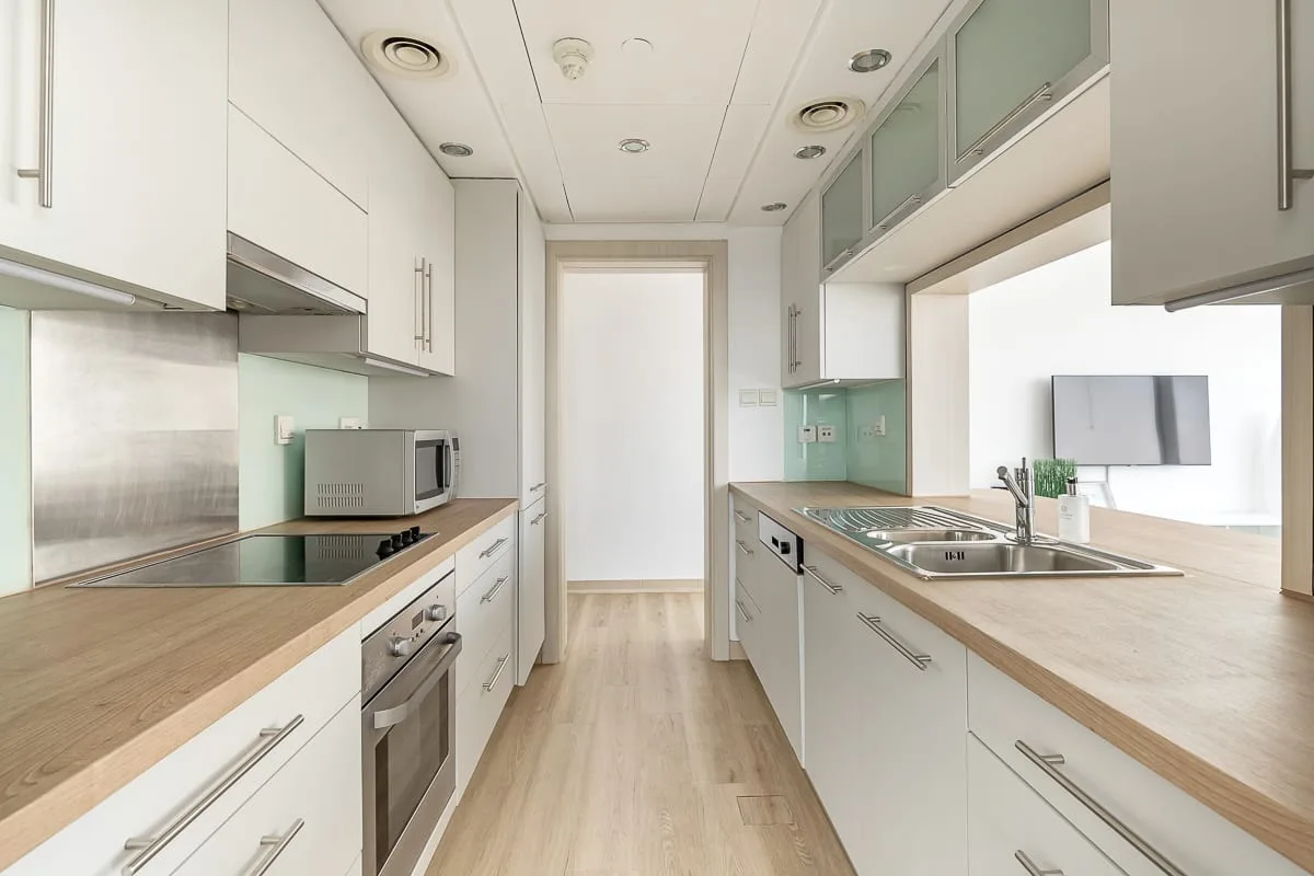 Una cocina tipo pasillo luminosa con encimeras claras y electrodomésticos de acero inoxidable.