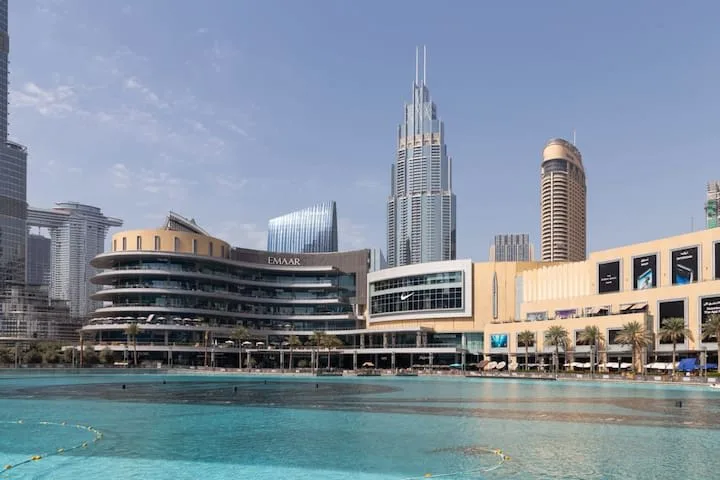 Una gran piscina al aire libre está frente a edificios modernos de gran altura y un centro comercial.