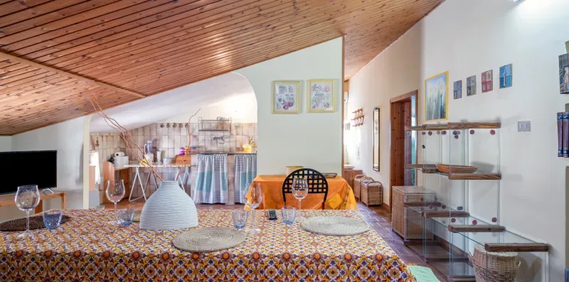 Un dormitorio con una colcha estampada, techo de madera inclinado y una pequeña cocina con cortinas.
