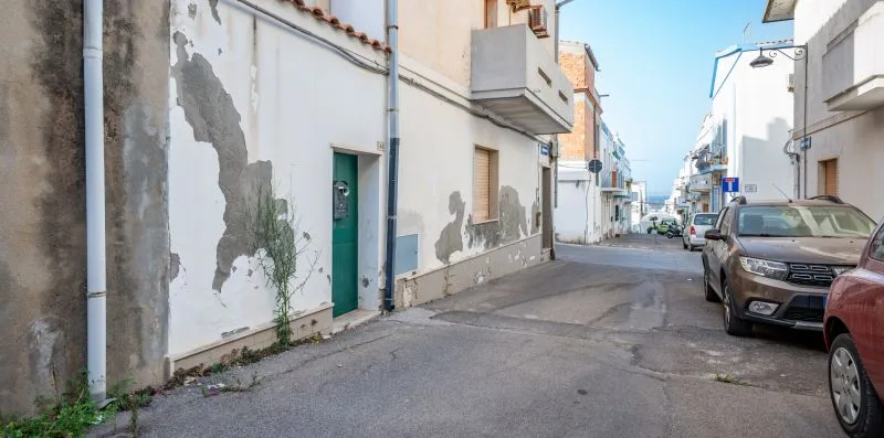 Una calle estrecha bordeada de edificios blancos y coches aparcados bajo un cielo despejado.