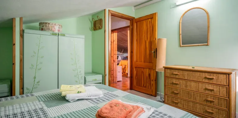 Dormitorio con cama, armario y cómoda de madera junto a una puerta abierta.
