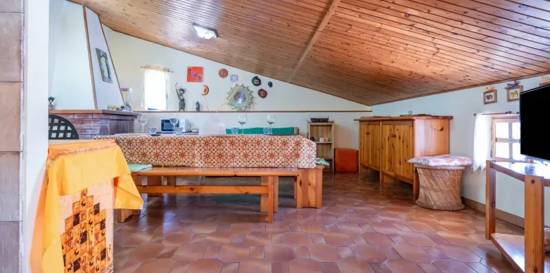 Un comedor rústico con mesas de madera, suelo de baldosas y techo inclinado.