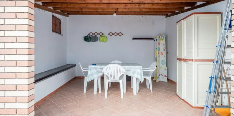 Un patio cubierto con una mesa y sillas blancas bajo vigas de madera expuestas.