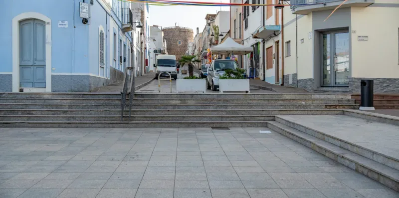 Una calle peatonal pavimentada, bordeada de edificios y vehículos estacionados.