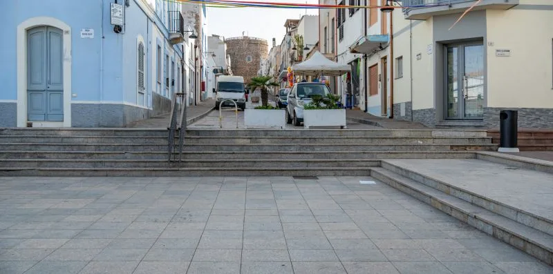 Una calle peatonal pavimentada con escalones entre edificios y asientos al aire libre.
