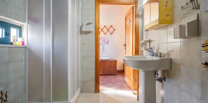 Un baño con lavabo y ducha, con una puerta abierta hacia un dormitorio.
