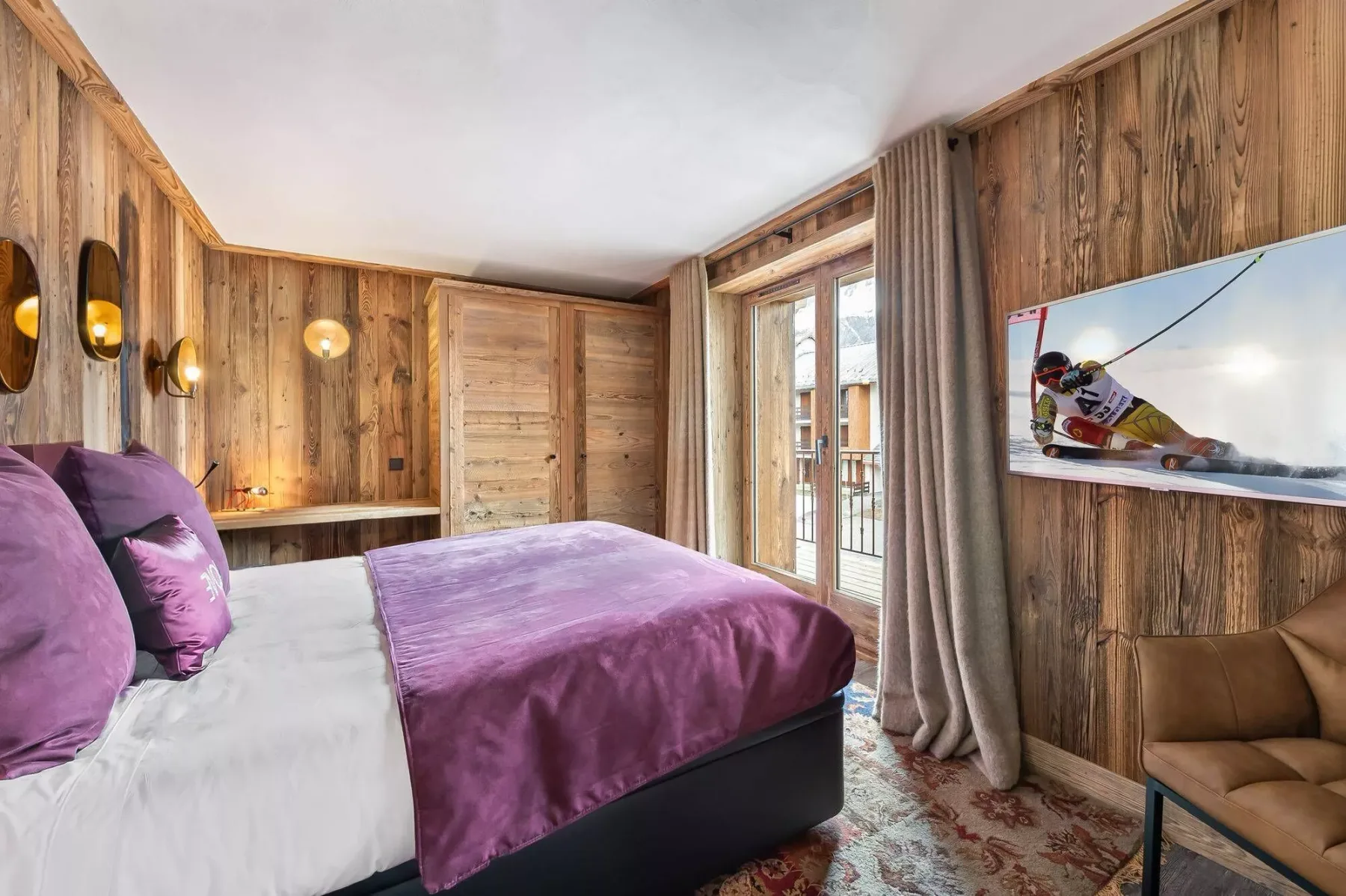 A bedroom with a purple bedspread, wood-paneled walls, and a glass door.